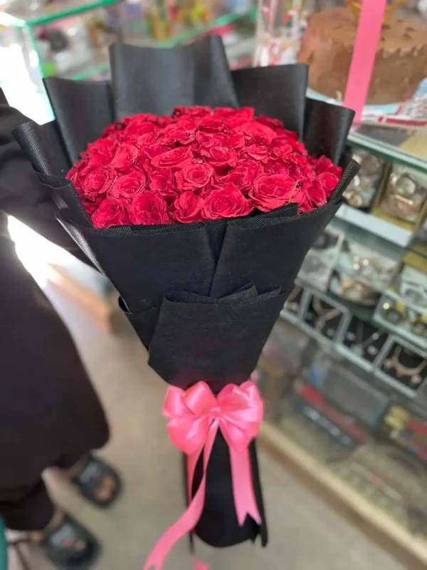 A luxury red roses bouquet arranged in elegant black matte wrapping with satin ribbon, fresh premium long-stem red roses, soft natural lighting, romantic and classy atmosphere, placed on a clean white marble background, ultra realistic flower details, luxury floral aesthetic, high-end product photography, shallow depth of field, minimal shadows, premium ecommerce style, 8K resolution, sharp focus, visually appealing for online gift store, modern luxury bouquet presentation, perfect for Valentine’s Day, anniversaries, birthdays, and romantic gifting